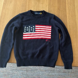 Mörkblå stickad tröja Polo Ralph Lauren - Mörkblå stickad tröja från Polo Ralph Lauren med amerikansk flagga. Väldigt bra skick knappast använd.