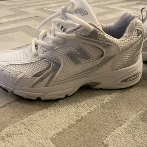 Vita New Balance 530 sneakers strl 38 - Säljer ett par fräscha New Balance 530 sneakers i vitt med silverdetaljer. Skorna har med ABZORB-dämpning. Perfekta för dig som gillar sportig och clean stil.