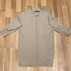 Beige tröja med dragkedja från J.Lindeberg - Säljer en stilren beige tröja från J.Lindeberg i storlek M. Tröjan har en dragkedja framtill och en klassisk krage. Perfekt för både vardag och lite mer uppklädda tillfällen. Den är i ett mjukt material som känns skönt mot huden. Passar perfekt till höst och vår!