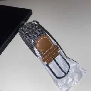 Flätat bälte  - Grått flätat bälte. Riktigt snyggt bälte som passar med dom flesta jeans. Bältet är elastiskt och passar i stort sett alla storlekar. Brunt läder som jag tycker är väldigt snyggt eftersom att det gör lite mer på bältet så att den inte ser såtråkigtut