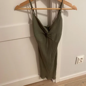 Olivgrön ribbad klänning - Säljer en superfin olivgrön klänning med ribbad struktur. Den har en snygg omlott-design framtill och smala axelband. Perfekt för sommardagar eller en avslappnad festkväll. Klänningen är i nyskick och har en tight passform som framhäver figuren.