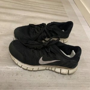 Svarta Nike sneakers - Säljer ett par svarta Nike sneakers med vit sula och den klassiska swoosh-loggan på sidan. Skorna har snörning. Använts ett par gånger, men de är fortfarande i bra skick för träning eller vardagsbruk. De är sköna att gå i.
