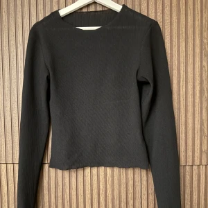 Svart ribbad långärmad topp  - Snygg svart ribbad topp med långa ärmar. Perfekt för en stilren look och passar till många olika outfits. Enkel och elegant design.