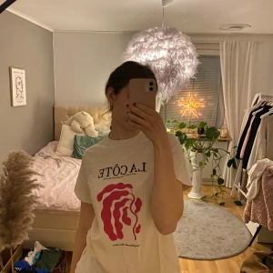 Vit t-shirt med tryck 'La Côte' - Säljer en vit t-shirt med trycket 'La Côte' i svart och ett abstrakt rött mönster på framsidan. Säljer då jag inte använder den längre. Passar de flesta då den är lite oversized.