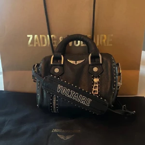 Svart handväska från Zadig & Voltaire - Kan tänka mig att gå ner lite i pris vid snabb affär! Snygg svart handväska från Zadig & Voltaire i skinn med coola nitar och en dekorativ logotyp. Väskan har både handtag och en avtagbar axelrem med texten 'VOLTAIRE'. Perfekt för att ge din outfit en edgy touch. I super fint skick och använd sparasmt. Är i en av Zadig s populäraste modeller.❤️❤️