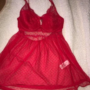 Röd spets babydoll från Hunkemöller - Säljer en röd babydoll från Hunkemöller med spetsdetaljer och prickigt mönster. Den har justerbara axelband och en transparent design som ger en elegant look. Perfekt för speciella tillfällen eller när du vill känna dig extra fin.