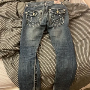 Blå jeans från True Religion - Snygga blå jeans från True Religion med unika bakfickor och kontrastsömmar. Jeansen har en klassisk femficksdesign och knappar med logotyp. Perfekta för en avslappnad stil.