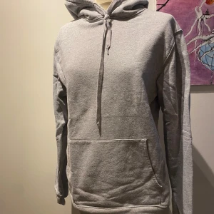 Grå hoodie - Säljer en stilren grå hoodie med justerbar dragsko i huvan och en praktisk magficka. Perfekt för en avslappnad look.
