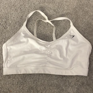 Vit sporttopp från Gymshark - Säljer en vit sporttopp från Gymshark med smala axelband och en enkel design. Perfekt för träning och bekväm passform.