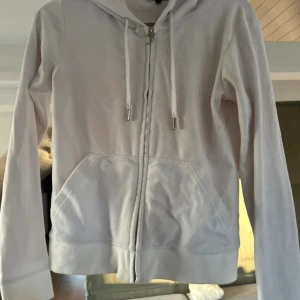 Juicy coture  - Säljer en stilren vit hoodie från Juicy Couture med dragkedja och logodetaljer. Hoodien har långa ärmar och en praktisk ficka framtill. Perfekt för en avslappnad look.