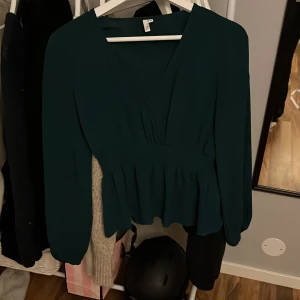 Mörkgrön omlottopp - Snygg mörkgrön omlottopp med långa ärmar och smockdetalj i midjan. Perfekt för en stilren look.