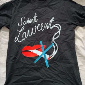 Svart t-shirt från Saint Laurent -  svart t-shirt från Saint Laurent med ett  tryck av röda läppar och en cigarett. Perfekt för en avslappnad stil med en touch av attityd. Kvitto finns ifall det önskas samt box och tags hör gärna av er angående frågor 