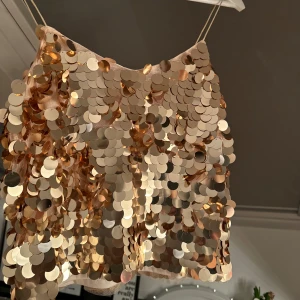Guldig paljett-tubtopp - Snygg guldig tubtopp täckt med glittrande paljetter. Perfekt för en festlig kväll eller nyårsfirande. Toppen har en croppad design och smala axelband.