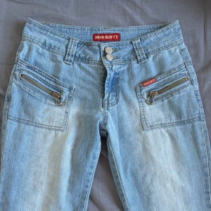 Ljusblå jeans med dragkedjedetaljer - Ljusblå jeans med dragkedjedetaljer framtill. Byxorna har en lågmidjad och straight passform. Köpta second hand men använda en gång av mig. Bra skick! Passar liten S och XS.