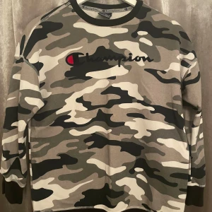 Camouflage tröja från Champion - Säljer en cool camouflage tröja från Champion strl 150/155 (11/12 år) med deras logga på bröstet. Tröjan har långa ärmar och en rund halsringning. Perfekt för en avslappnad stil.