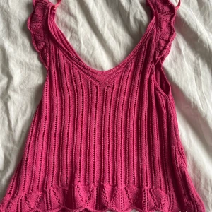 Rosa stickad topp från ONLY - Säljer en söt rosa stickad topp från ONLY i storlek XS. Toppen har en v-ringad design med volangdetaljer vid axlarna och en ribbad struktur. Perfekt för en somrig look!
