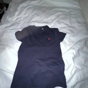 Ralph lauren t shirt - Snygg mörkblå t-shirt från Ralph Lauren med en röd broderad logga på bröstet. Perfekt för en stilren och avslappnad look. Passar om du är runt 160-170 ( beroende på vikt kan den passa både längre och kortare👍 tröjan är u använt skick men har inga defekter, det ända man kan se att den har använts på är att texten högst upp på t shirten (mott macken) är borta annars topp skick. 