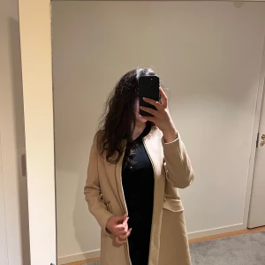 Beige kappa - Snygg beige kappa med klassisk design. Perfekt för höst och vår, med en stilren look som passar till många outfits. Kappan har långa ärmar och en rak passform. Kappan är ifrån Hm och är i storlek 34!