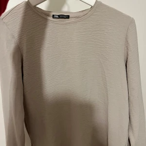 Beige långärmad tröja från Zara - Säljer en stilren beige långärmad tröja från Zara. Perfekt för en avslappnad look med sin mjuka och bekväma passform. Tröjan har en enkel design som gör den lätt att matcha med olika outfits. Storlek S