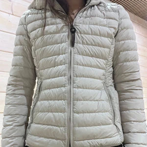 Beige pufferjacka från Parajumpers - Säljer en snygg beige pufferjacka från Parajumpers. Jackan har en dragkedja framtill och en praktisk huva. Perfekt för kyliga dagar med sin quiltade design som håller värmen.