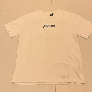 Vit t-shirt med tryck - Säljer en vit t-shirt från Black Squad. Baksidan har även ett stort korsmotiv. T-shirten har en relaxed fit och är kortärmad.