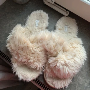Beiga fluffiga tofflor från Gina Tricot - Mysiga beiga tofflor med fluffigt pälsmaterial. Perfekta för att hålla fötterna varma och bekväma inomhus. Sulan är slät och ger bra grepp på golvet. Köpta från Gina Tricot, använda fåtal gånger men säljer då jag har många tofflor så dessa använder jag inte. Går att tvätta i tvättmaskin! Hör av vid frågor, pris kan diskuteras ❤️