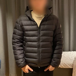 Svart pufferjacka med huva - Säljer en svart pufferjacka med huva. Jackan har en dragkedja framtill och är långärmad. Perfekt för kyligare väder.