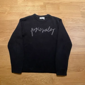 Svart tröja från Weekday - Säljer en svart tröja från Weekday med texten 'magic reality' broderad på framsidan. Tröjan har en rund halsringning och långa ärmar. Perfekt för en stilren och avslappnad look.
