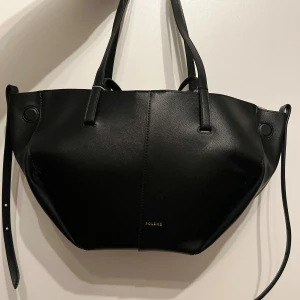 Svart handväska från Polene  - Elegant svart handväska från Polène i skinn. Väskan har en stilren design med två handtag och en praktisk innerficka med dragkedja. Perfekt för att bära dina dagliga nödvändigheter med stil.