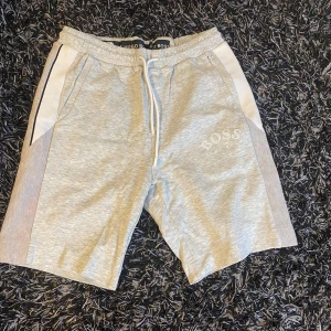 Grå shorts från Hugo Boss - Snygga grå shorts från Hugo Boss med vit detalj på sidorna och logga på benet. De har en bekväm resårmidja med snörning för justerbar passform.
