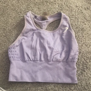 Ljuslila sporttopp från Gymshark - Säljer en ljuslila sporttopp från Gymshark med ribbad nederkant och snygga meshdetaljer på sidorna. Toppen har en brottarrygg för extra stöd och komfort under träning. Perfekt för gymmet eller yoga!