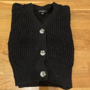 Svart stickad kofta från XOXO Friends - Säljer en svart stickad kofta från XOXO Friends med stora knappar framtill. Koftan har en mysig och ribbad design, perfekt för kyligare dagar. Den är långärmad och har en klassisk passform.