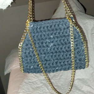 Jeansblå virkad väska med guldkedja - Snygg jeansblå virkad väska med en elegant guldkedja.Väskan har en unik textur och är perfekt för att ge din outfit en trendig touch. Den är rymlig nog för dina dagliga nödvändigheter och passar bra till både vardag och speciella tillfällen.