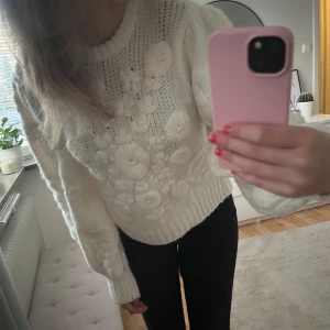 Vit stickad tröja med blommönster - Mysig vit stickad tröja med ett vackert blommönster. Tröjan har långa ärmar och ribbade muddar vid ärmslut och nederkant. Perfekt för kyliga dagar💕💕