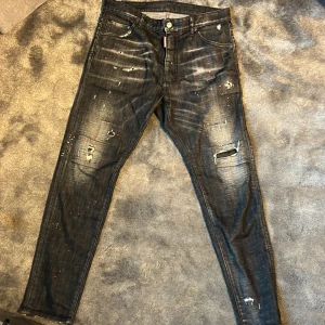 Svarta jeans med slitningar - Snygga svarta jeans med coola slitningar och röda färgstänk. De har en klassisk femficksdesign och knappgylf. Perfekta för en edgy look.