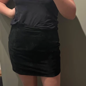 Vintage Svart mockakjol - Säljer en stilren svart mockakjol i kort modell. Perfekt för både vardag och fest! Kjolen har en enkel design med knapp och dragkedja bak. Den är i bra skick och passar till många olika outfits.  Midja 42 cm Längd 45 cm  Superfin till höst och vinter med ett par snygga stövlar.