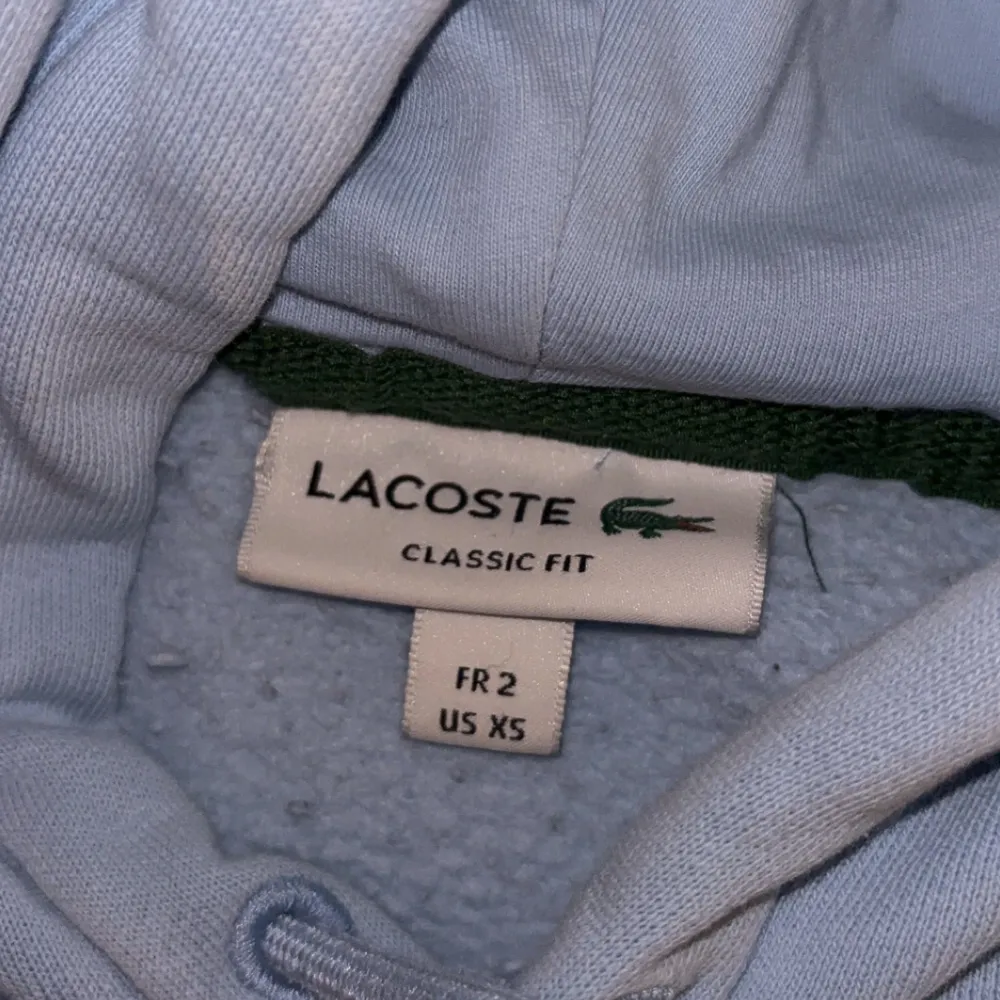 Säljer en Lacoste Hoodie i storlek XS. Ljusblå färg med Lacoste loggan på bröstet. Använd en gång. Bättre pris vid snabb affär. Funkar för alla årstider! Nypris 1750 kr.. Tröjor & Koftor.