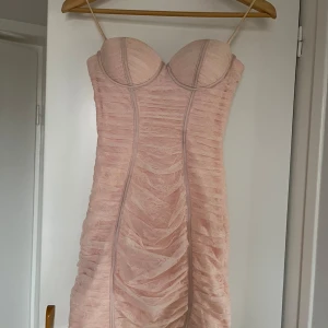 Ljusrosa tight klänning - Säljer en superfin ljusrosa klänning i tight passform. Den har en snygg rynkad design och smala axelband. Perfekt för fest eller en utekväll! Klänningen är i mycket bra skick och har en dragkedja bak för enkel påklädning.