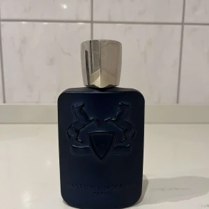  Parfums de Marly Layton - Säljer en elegant och lyxig parfym från Parfums de Marly, modell Layton. Flaskan är mörkblå med en stilren design och har en silverfärgad kork. Den kommer i en snygg mörkblå kartong med vita ränder och detaljer. Perfekt för den som vill ha en sofistikerad doft med en touch av kunglig elegans. Det finns 100ml kvar i flaskan. Och priset kan snackas vid en snabb affär. Självklart är den äkta.