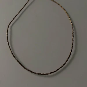 Guldigt halsband med små pärlor - Ett enkelt och stilrent halsband i guld med små pärlor. Perfekt för att lägga till en touch av elegans till vilken outfit som helst. Passar både till vardags och festliga tillfällen.