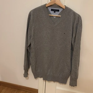 Grå tröja | Tommy Hilfiger - Säljer en stilren grå tröja från Tommy Hilfiger i storlek M. Den har en klassisk v-ringning och är perfekt för både vardag och lite finare tillfällen. Tröjan är i mycket bra skick och passar perfekt till höst och vår. 