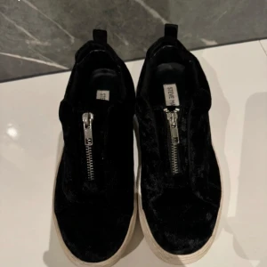 Svarta sneakers från Steve Madden - Säljer ett par svarta sneakers från Steve Madden i bra skick. De har en snygg dragkedja på ovansidan och en vit sula som ger en cool kontrast. Perfekta för både vardag och fest! 🖤