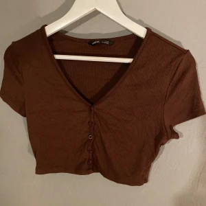 Brun ribbad topp från Shein - Säljer en brun ribbad topp från Shein i storlek S. Den är kortärmad och har en v-ringad design med knappar framtill. Perfekt för en avslappnad sommarlook eller att styla med lager under hösten. (PM OM DU VILL HA FLER BILDER)