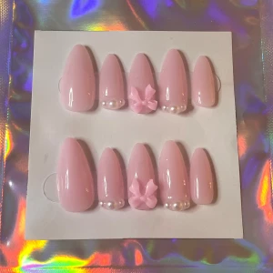 Rosa lösnaglar med pärldekoration - Säljer ett set med supergulliga rosa lösnaglar. De har en fin glansig finish och är dekorerade med små pärlor och en söt rosett på några av naglarna. Perfekt för en söt och stilren look! 💅🎀