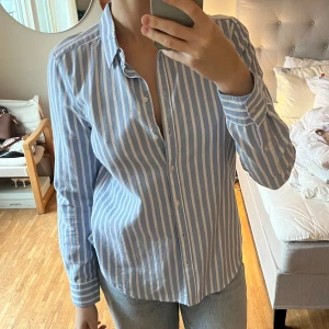 Blåvit randig skjorta från Gina Tricot - Säljer en snygg blåvit randig skjorta från Gina Tricot i storlek 38 men är mer som en S. Skjortan har långa ärmar och knappar framtill.😊