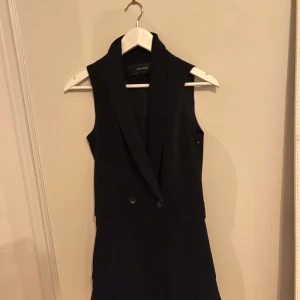 Svart västklänning från Zara Basic - Snygg svart västklänning från Zara Basic i mycket bra skick. Den har en elegant krage och knappar framtill. Perfekt för både fest och vardag. Passar bra till höst och vår.