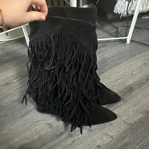 Svarta mockastövlar med fransar - Säljer ett par svarta stövlar i mocka med snygga fransdetaljer. De har en spetsig tå och är perfekta för höst och vinter. Stövlarna är i mycket bra skick och en perfekt detalj till alla outfits! De är från HM och originalpris är 1500