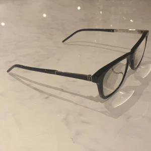 Svarta glasögon från Saint Laurent - Säljer ett par stilrena svarta glasögon från Saint Laurent. De har en klassisk rektangulär form och är perfekta för både vardag och fest. Ramen är i ett elegant svart material som ger en tidlös look. Passar perfekt för dig som vill ha en touch av lyx i din stil. 🖤