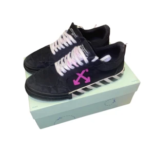 Svarta sneakers från Off-White - Säljer ett par snygga svarta sneakers från Off-White i mycket bra skick. De har vita snören och en cool rosa pil-design på sidan. Sulan har ett randigt mönster i svart och vitt. Perfekta för att ge din outfit en trendig touch!