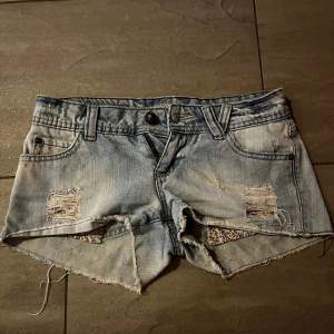 Säljer ett par ljusa lågmidjade jeansshorts med coola slitningar och råa kanter. De har en avslappnad look med blommigt tyg som syns genom slitningarna. Perfekta för sommardagar! 🩷🫶🏼. Midjemåttet tvärs över är 39cm